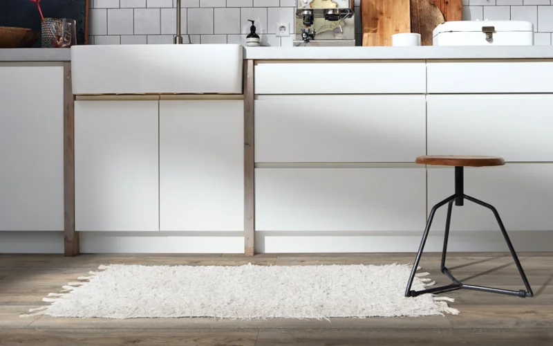 Moderne Küche mit weißen Fronten, Holzboden, Teppich und Hocker