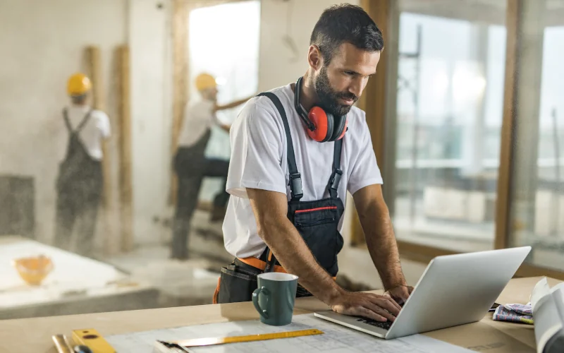 Handwerker am Laptop auf einer Baustelle
