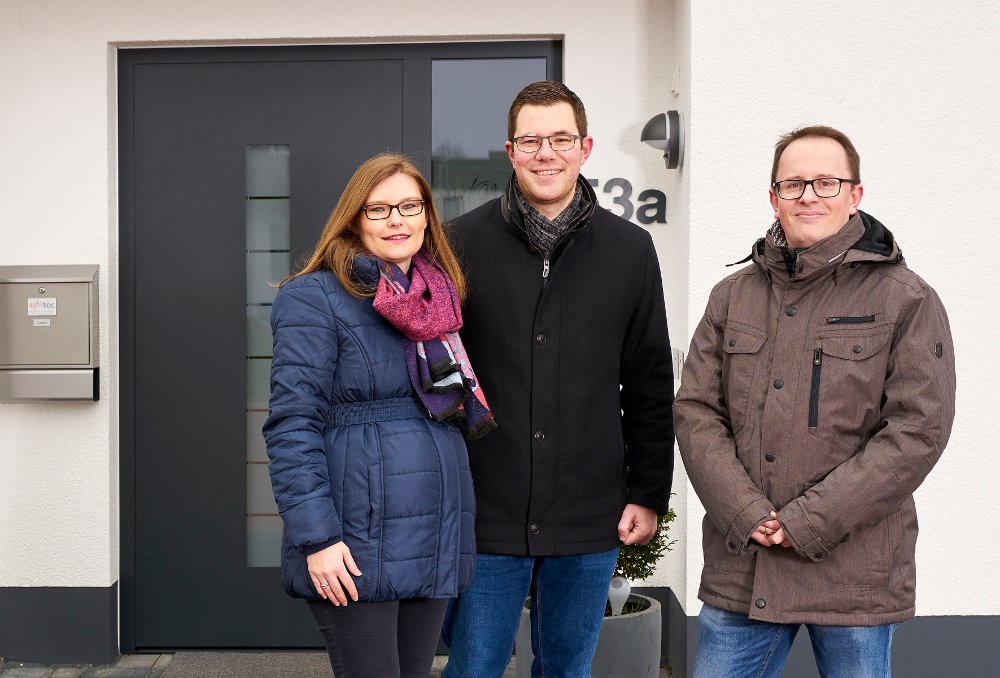 Paar mit einem Berater vor grauer Haustür