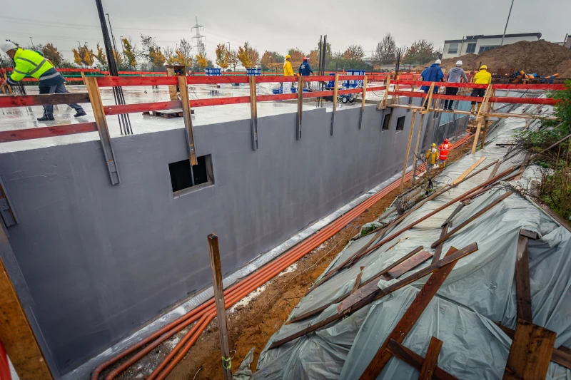 Betonrohbau mit Bewehrung für Decke, Baustelle mit Absturzsicherung und Arbeiter.