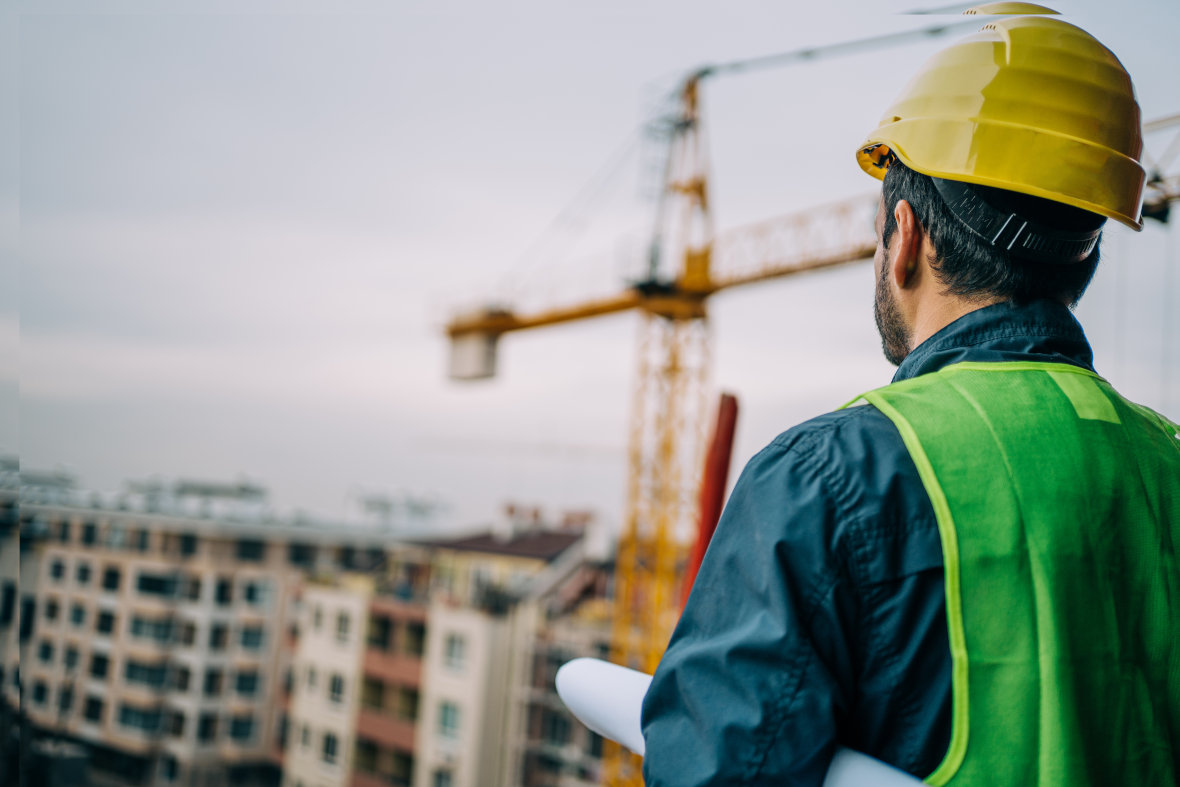 Mann in Warnweste schaut über Baustelle mit Kran