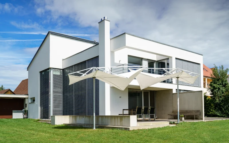 weißes modernes Wohnhaus mit Jalousien und Sonnensegel als Sonnenschutz