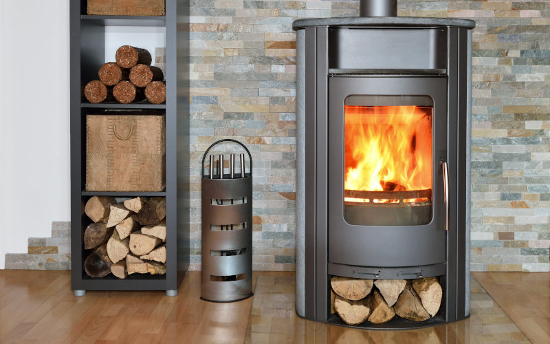 Moderner Kaminofen mit brennendem Feuer, Holzlager daneben.