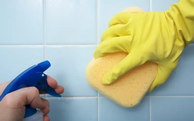 Mann putzt Fliesenwand mit Reiniger und Lappen