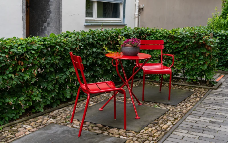 rote Metall-Gartenmöbel bestehend aus Tisch und Stühlen neben einer Hecke