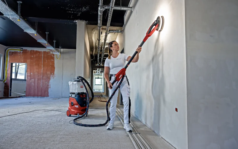 Frau saugt eine Wand mit einem Sicherheitsstaubsauger von FLEX ab