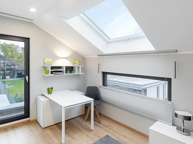 Ein Büro mit Terrassentür, Schreibtisch, Stuhl und Regalen mit einem großen Heiz-Dachfenster schräg über dem Schreibtisch.