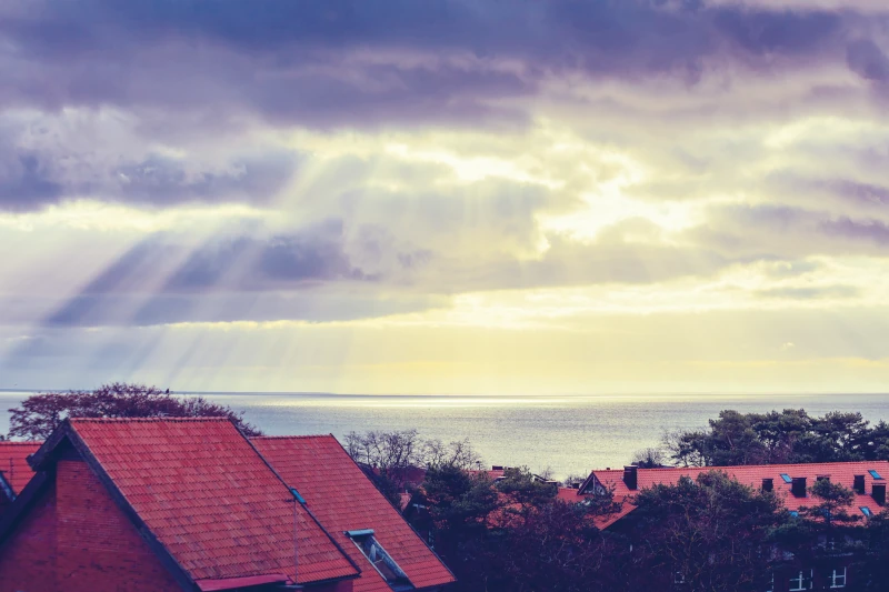 Hausdächer und Meer mit Sonne die die Wolken Durchbricht im Hintergrund
