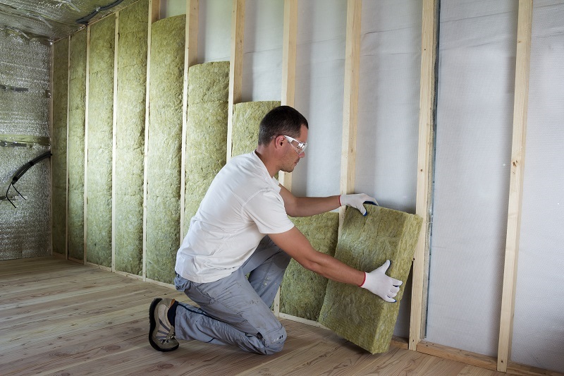Mann bringt Dämmplatten in Holzkonstruktion an der Wand an