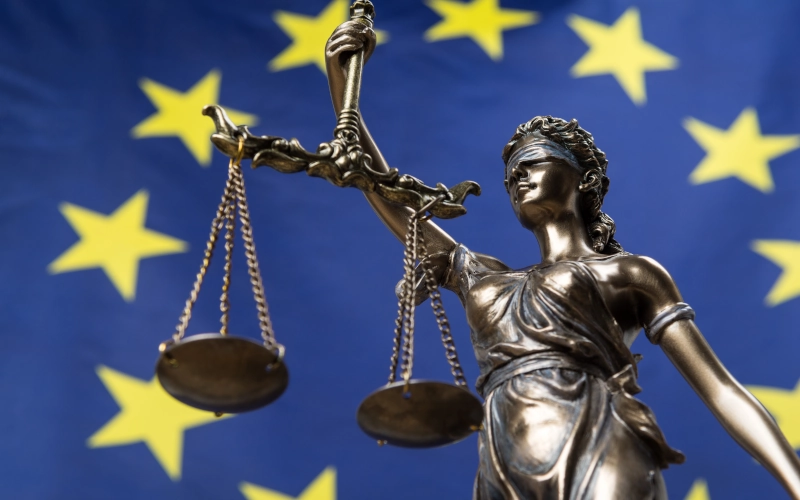 Statue der Göttin der Gerechtigkeit Themis oder Justitia, gegen eine europäische Flagge, als ein Rechtsbegriff mit verbundenen Augen