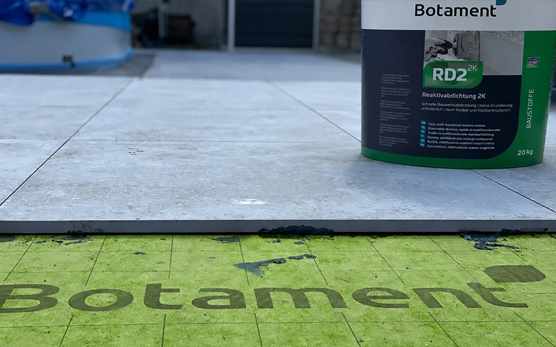 Gebinde mit Reaktivabdichtung 2K von Botament steht auf verlegten Fliesen