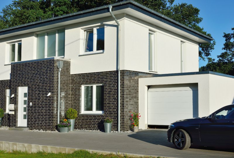 Mehrfamilienhaus in weiß und Backstein mit Garage und Auto davor