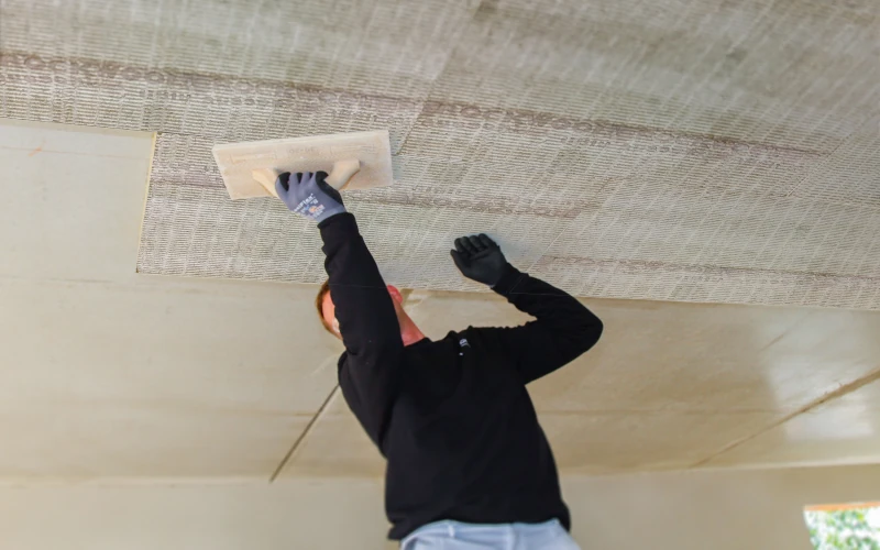Handwerker drückt Dämmmaterial an die vorher mit Kleber vorbereiteten Stellen der Kellerdecke