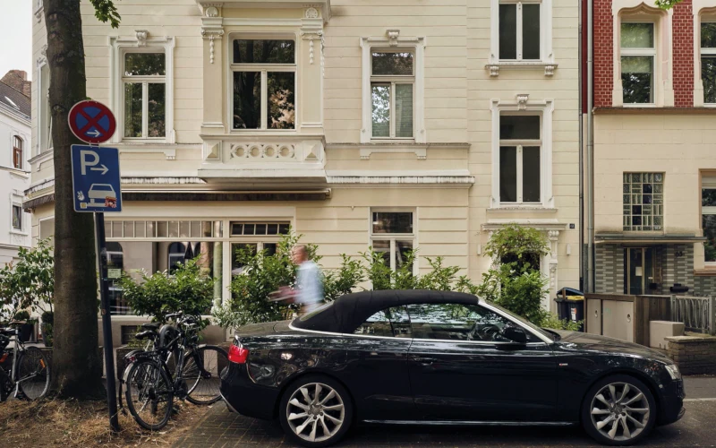 Fotoaufnahme von einem Auto mit einem Gebäude hinter und Fahrrädern an der Seite.