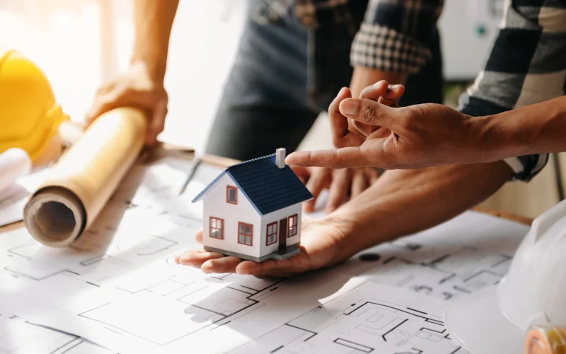 zwei Menschen planen ein Haus an einem Tisch mit Bauplänen ausgelegt