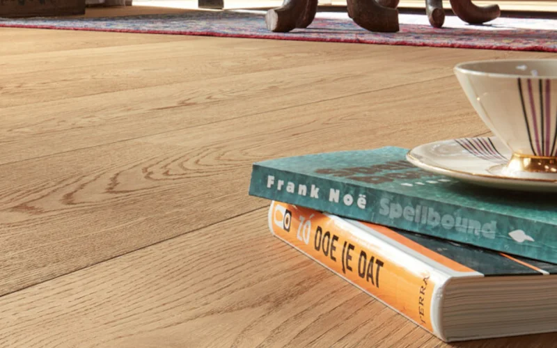 heller Holzfußboden mit Büchern und einer Tasse daraufliegend