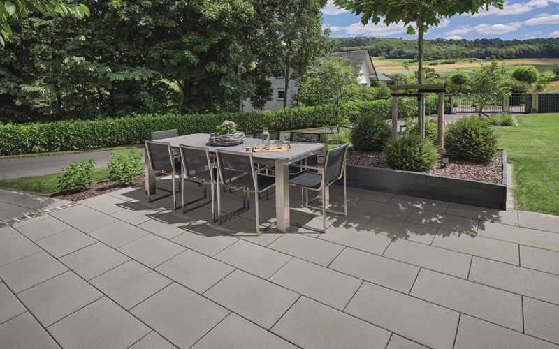 Terrasse mit grauen Platten und Gartenmöbeln und Hecke im Hintergrund