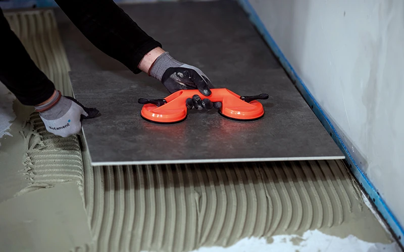Handwerker setzt eine Fliese auf einen Untergrund mit Fliesenkleber