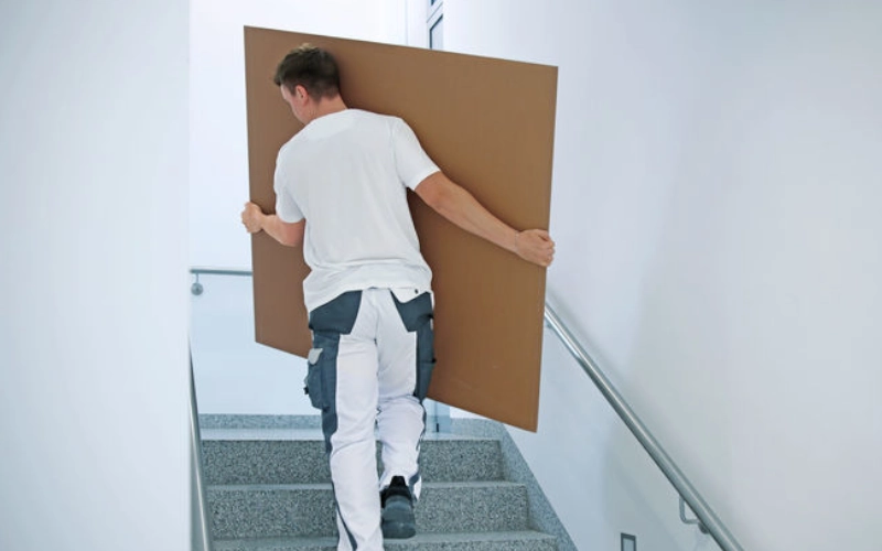 Junger Handwerker trägt die Schallschutzplatte Silentboard 2in1 der Firma Knauf die Treppe hinauf.