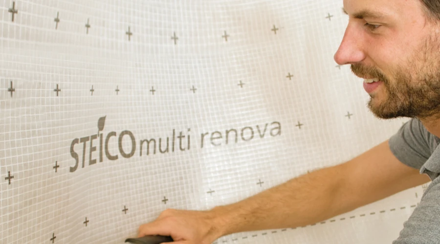 Ein Mann bringt eine Folie mit der Aufschrift „STEICO multi renova“ an der Wand an.