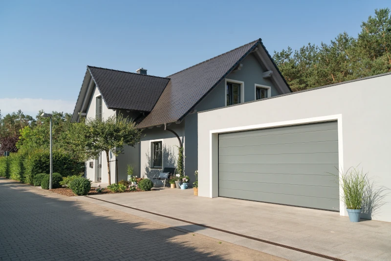 Neben einem Haus ist eine Garage aufgestellt mit einem grün-gräulichem Garagentor