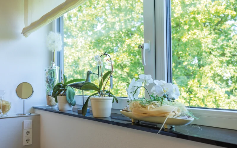 Fensterbank an großen Fenstern mit Blumen und Deko bestückt