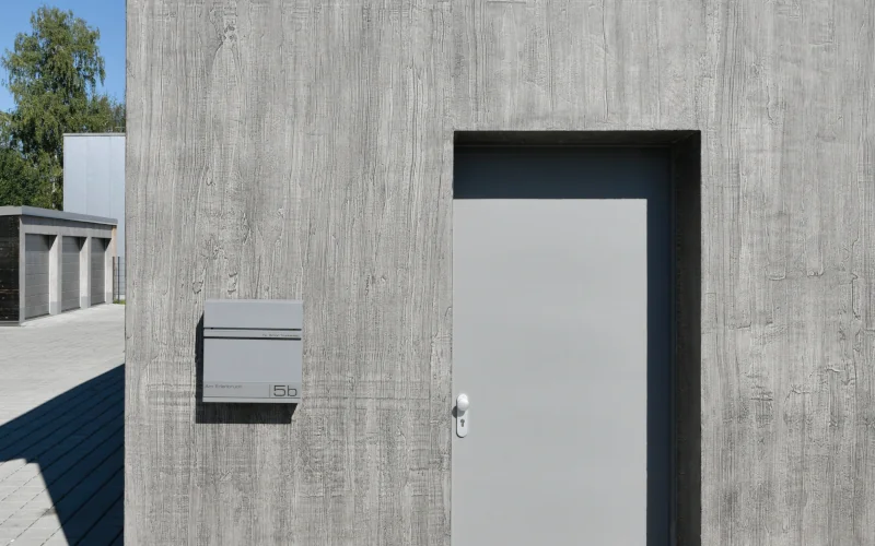 Haus mit grauer Betonfassade, grauer Tür und grauem Briefkasten