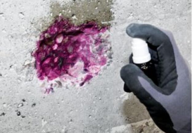 Hand mit Handschuhen sprüht lila Indikatorlösung auf Betonoberfläche.