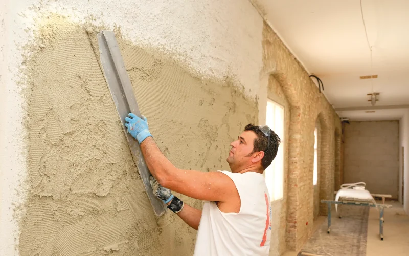 Handwerker glättet Dämmputz an einer Wand mit einem Richtscheit