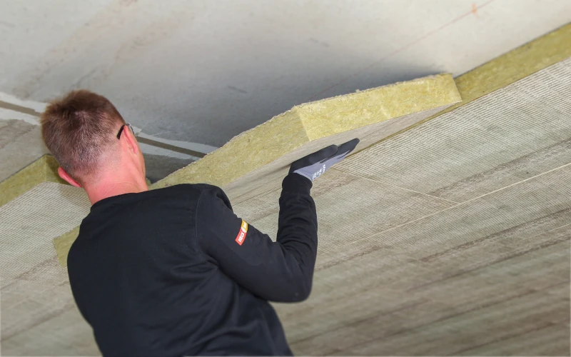 Handwerker der Dämmmaterial an einer Kellerdecke positioniert