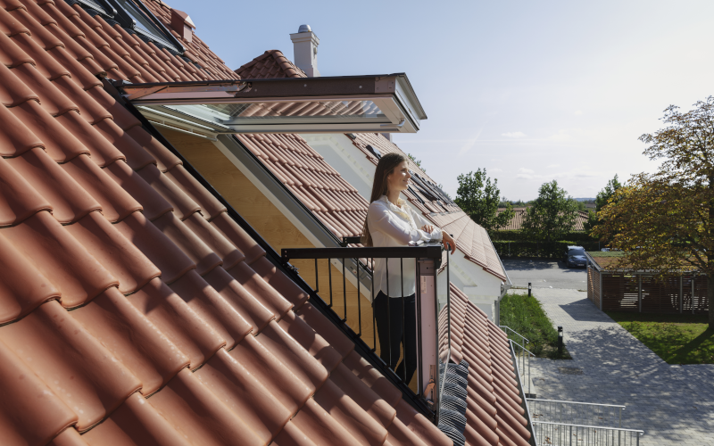 Frau steht an einem Dachfenster mit begehbarem Balkon