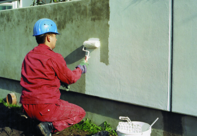 Ein Handwerker trägt Farbe an Betonwand auf