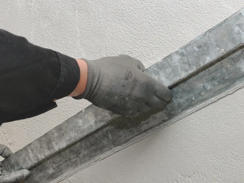 Mit einem metallischen Abzieher wird eine Wand geglättet.