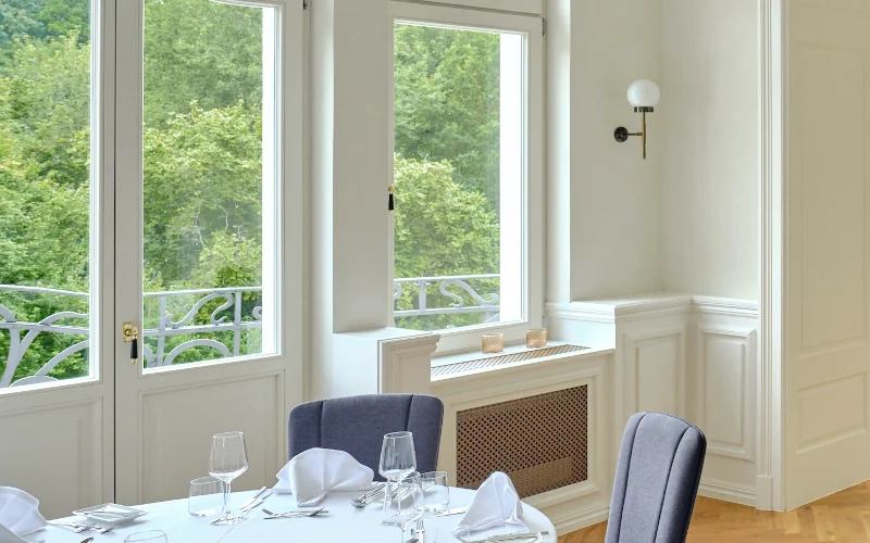 Wohnraum eines Altbaus mit gedecktem Tisch mit vielen Fenstern, weißen Wänden und Bordüre
