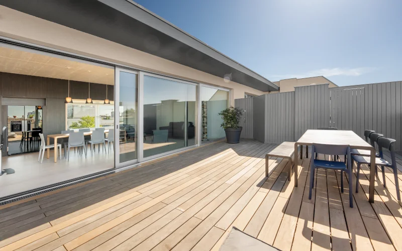 Moderne Terrasse mit Holzboden, großer Fensterfront und Esstisch.