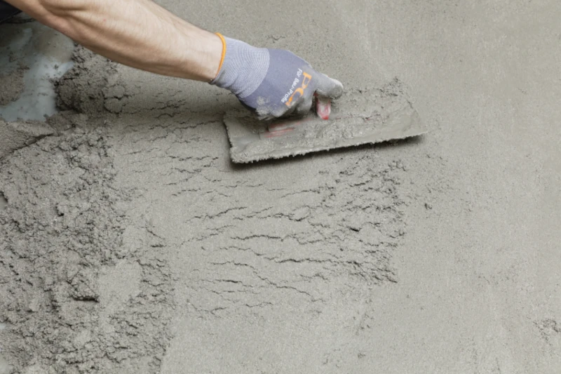 Hand mit Handschuh glättet Zementoberfläche mit Kelle.