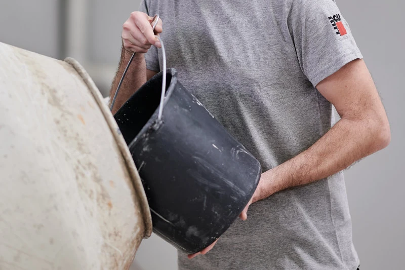 Handwerker kippt Inhalt eines Eimers in einen Betonmischer