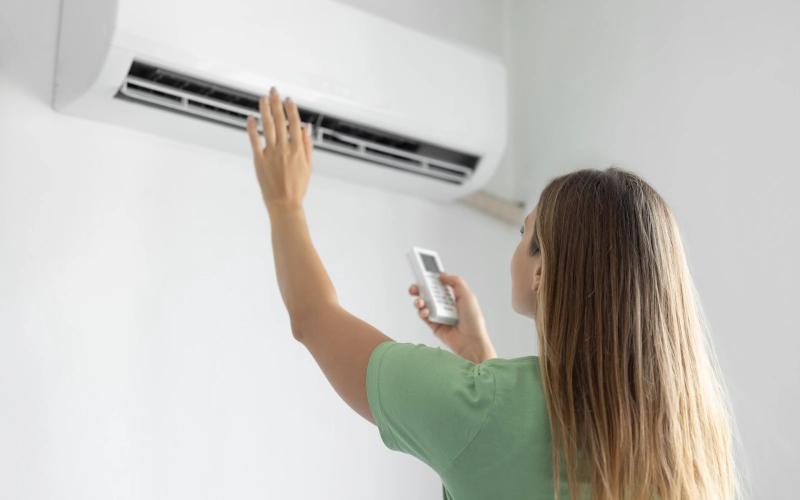 Frau schaltet Klimaanlage mit Fernbedienung ein