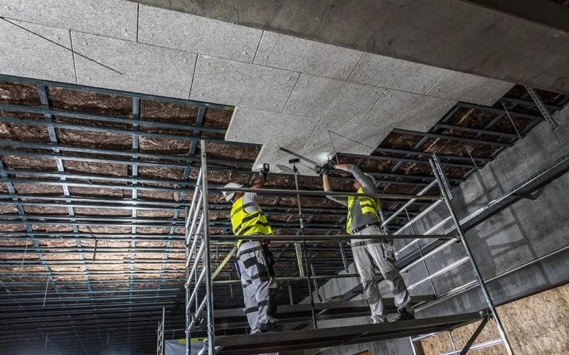 Arbeiter auf Gerüst montieren Dämmplatten an Tragprofilen an der Decke