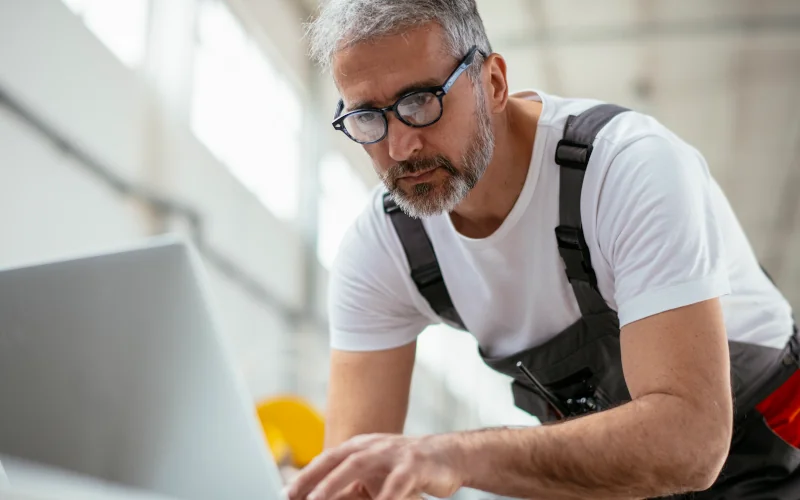 Handwerker steht an einem Laptop in einer Werkstatt