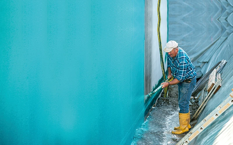 Bauarbeiter dichtet Kellerfassade mit Reaktivabdichtung ab