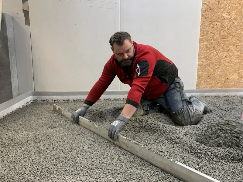 Mann streicht körnige Masse mit einem Richtscheit glatt