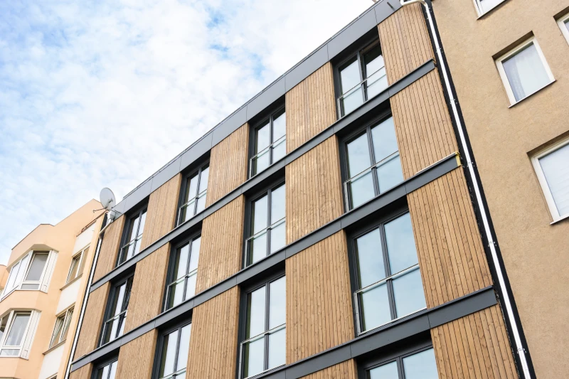 Blick von unten auf eine mit Holz und großen Fenstern sanierte Fassade an einem hohen Altbau.