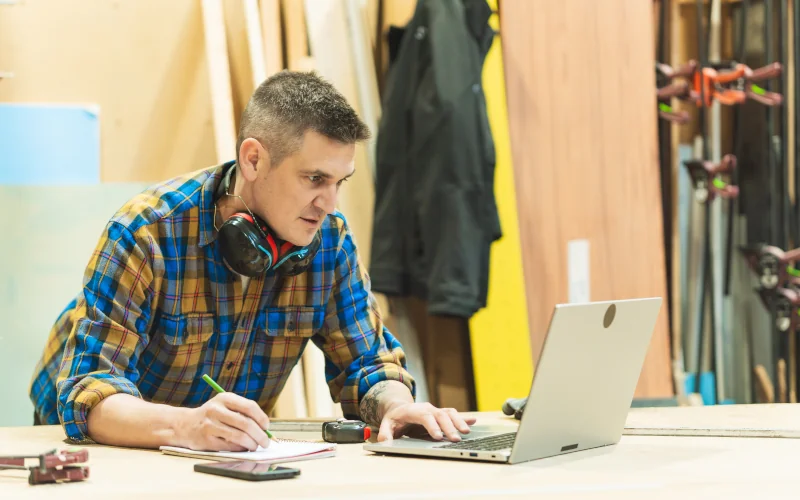 Handwerker in einer Werkstatt rechnet an seinem Laptop einen Kundenauftrag durch