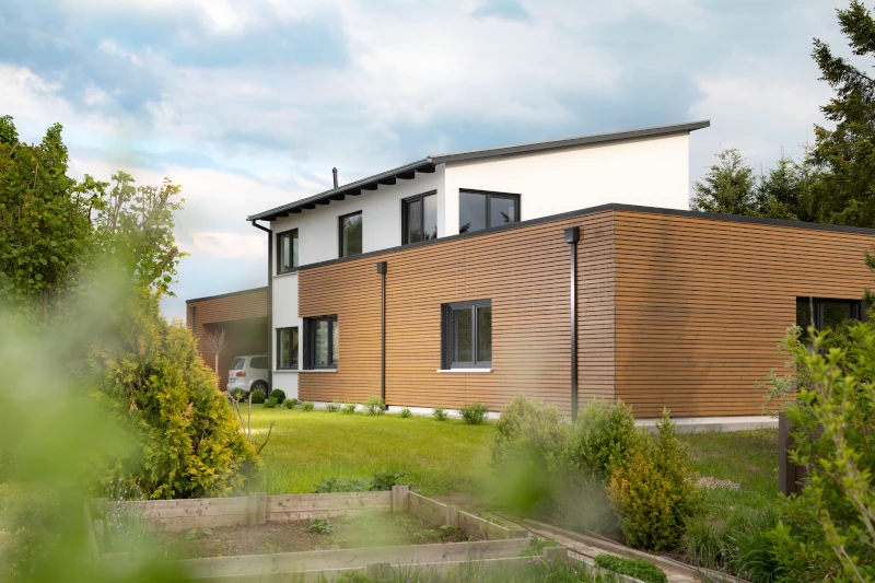 Ein modernes Einfamilienhaus. Die untere Etage ist mit einer vertikal angebrachten Holzfassade vor der Witterung geschützt.