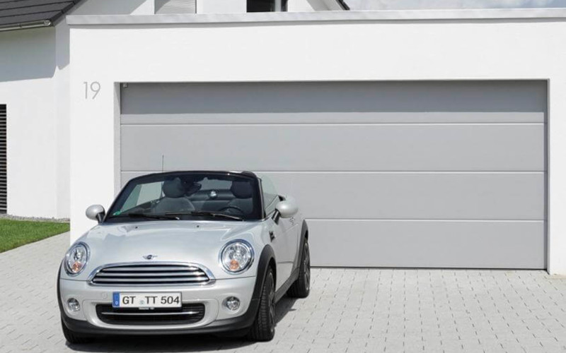 Mini steht auf Auffahrt vor einem hellgrauen Garagentor