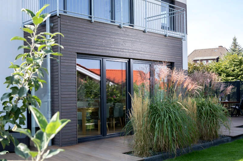 Ein kleines Stückchen eines modernen Einfamilienhauses. Die Fassade an der Terrasse ist durch vertikal angebrachte Profilhölzer vor der Witterung geschützt.