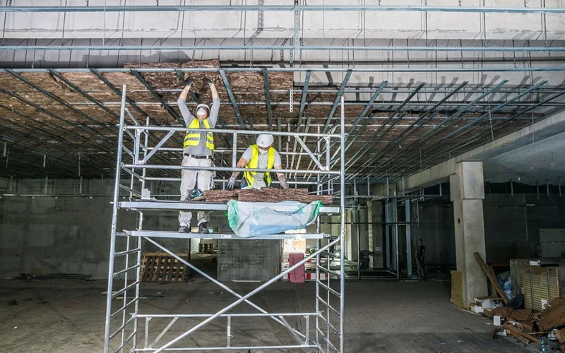 Arbeiter auf Gerüst befüllen abgehängte Decke mit Dämmauflage