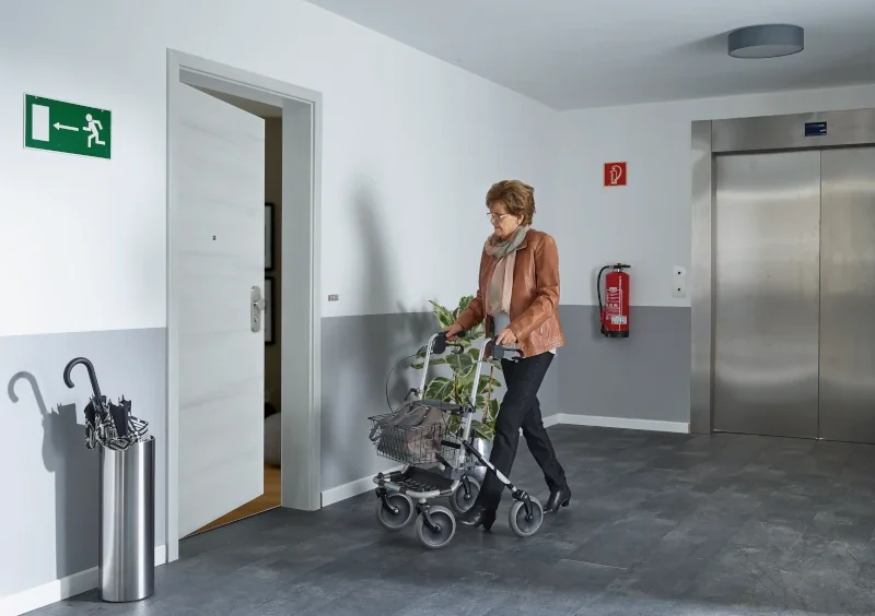 Frau mit einem Rollator öffnet eine barrierefreie Tür mit einer smarten Steuerung