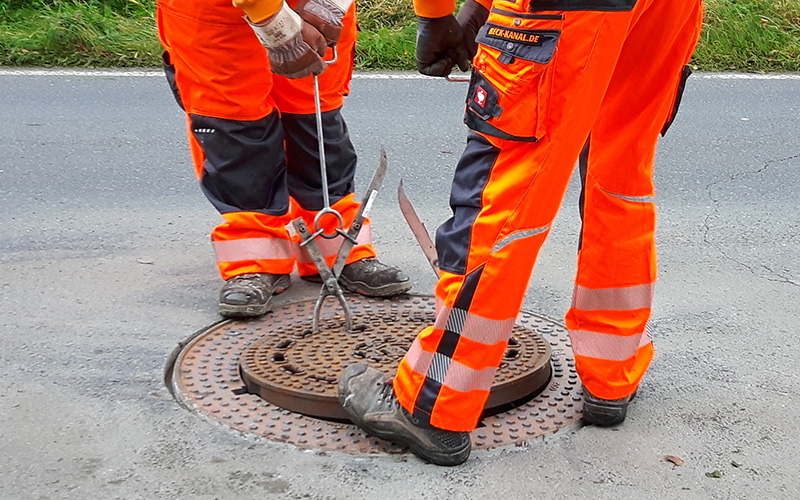 Zwei Bauarbeiter heben eine Gully Abdeckung hoch